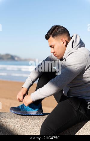 Young latin man tying laces before training. Focus and determination on sports concept. Stock Photo