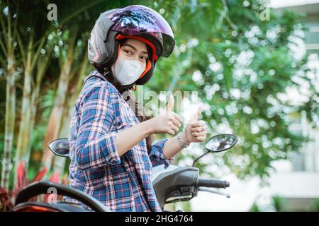 woman wearing helmet and mask with thumbs up on motorbike Stock Photo