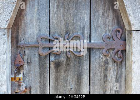Forged antique hinge covered with rust with a closing mechanism on a fragment of an old wooden door. Close-up. copy space. Stock Photo