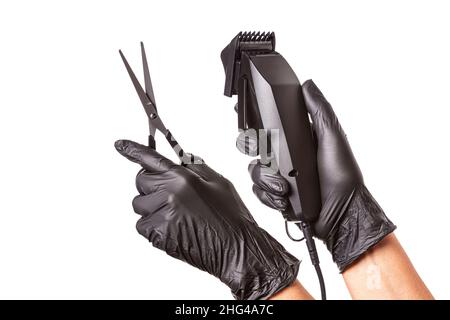 Hairdressers hands in black rubber gloves holds hair clipper and scissors. Isolated on white background, close up Stock Photo
