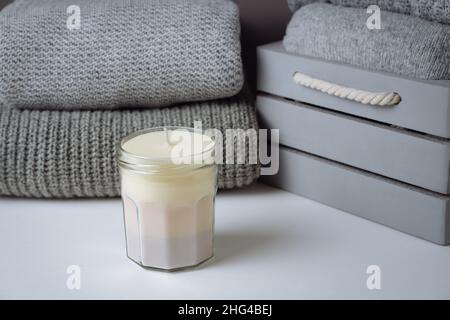 homemade scented multicoloured beige candle in mason jar with gray knit sweaters in a wooden box. Handmade craft organic gift. Monochrome product adve Stock Photo