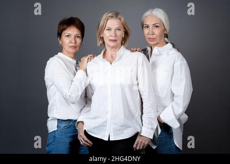 Portrait of beautiful mature women in white shirts posing at camera against the grey background Stock Photo