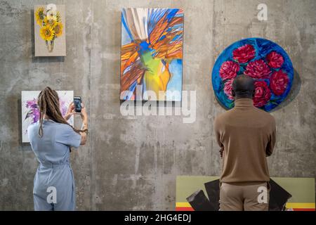 Back view of intercultural visitors of art gallery standing in front of wall with paintings while one of them photographing abstract picture Stock Photo