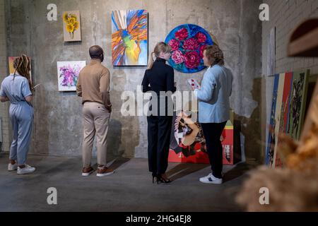 Young blond woman in black casualwear talking to mature elegant man among visitors of contemporary art gallery Stock Photo