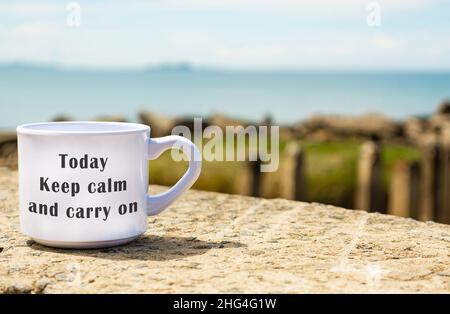 Motivational and Inspirational quote on a coffee cup with blurred beach background - Today Keep calm and carry on Stock Photo