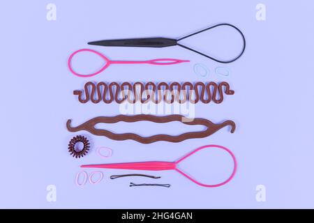 Various hair styling tools like bun maker, braid tool, ponytail style maker, hair clip, rubber bands and pins on violet background Stock Photo
