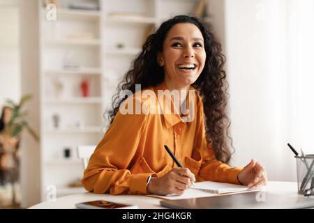 Happy Lady Taking Notes Sitting At Desk Holding Pen Indoor Stock Photo