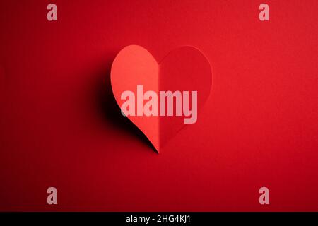Creative Valentines Day postcard design with red paper heart on red cardboard background. Valentine day and love concept Stock Photo