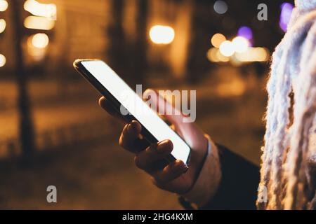 Close-up female hand holding modern smartphone on city street at night Stock Photo