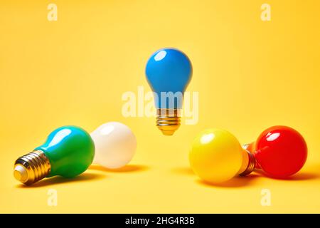Creative layout with multicolored lightbulbs on yellow background. Blue light bulb levitate in air. Idea symbol, business creativity, inspiration, bra Stock Photo