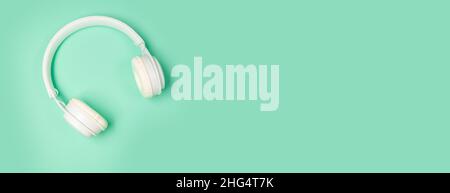 Studio shot of modern white wireless headphones isolated on green mint background. Music or podcast background Stock Photo