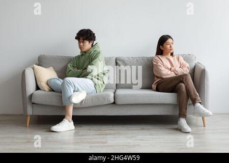 Annoyed young Asian couple sitting on couch in silence after fight, looking in opposite directions at home Stock Photo