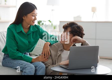 Happy young Asian couple using laptop, watching videos or shopping online, checking social media at home Stock Photo