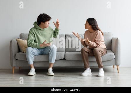 Breakup and divorce concept. Young married Asian couple having fight, yelling at each other in living room