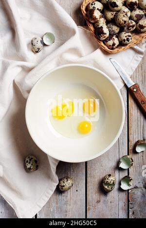 Broken quail eggs in a bowl on a wooden table. Stock Photo