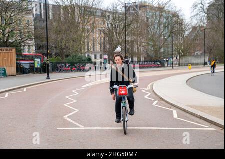 Man riding his bicycle around London Hyde park with a seagull on his head and a pigeon on his shoulder Stock Photo