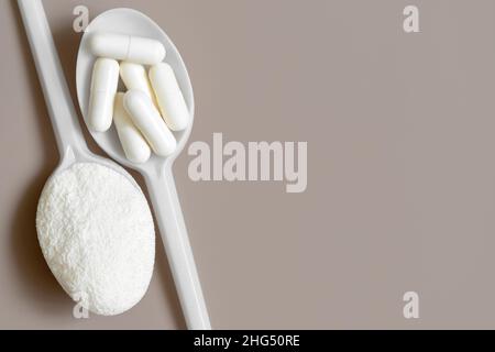 Collagen powder and pills on a beige background close up. Collagen in white measuring spoons. View from above. Space for text. Stock Photo