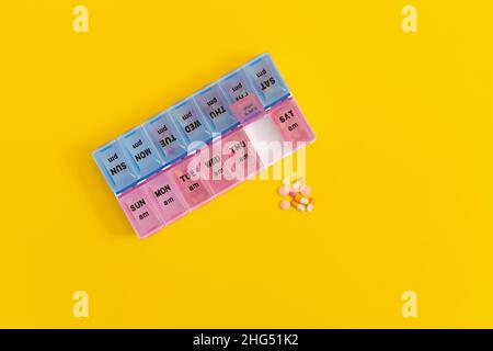 Daily pill box with medical pills on yellow background. Stock Photo