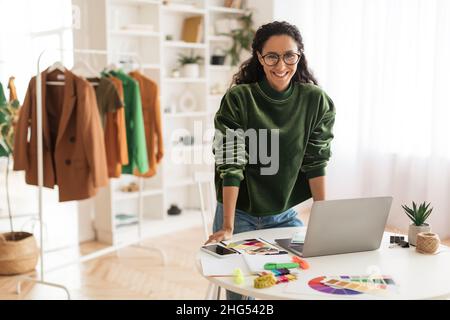 Happy Clothing Designer Lady Using Laptop Smiling Standing In Showroom Stock Photo