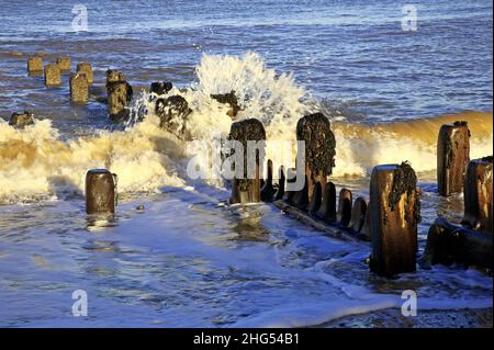 Wave breaking on an old timber breakwater sea defence on the North Norfolk coast at Cart Gap, Happisburgh, Norfolk, England, United Kingdom. Stock Photo