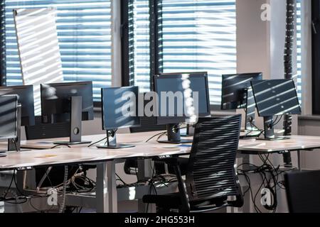 Office closed and empty due to the Covid or Coronavirus pandemic, with computers, chairs and desks in the shadow of a closed windows and curtains Stock Photo