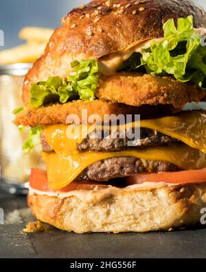 A very large burger with two crispy chicken patties, two bovine meat patties, slices of cheddar cheese, fresh lettuce and two tomato slices Stock Photo