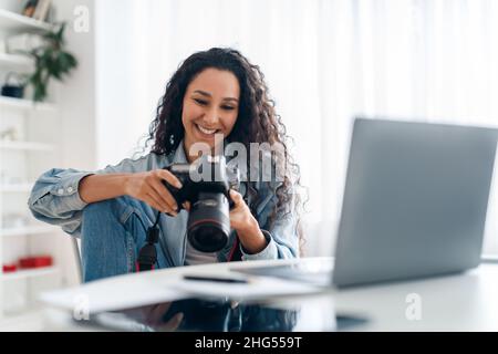 Female Photographer Holding Camera Looking At Photos Using Laptop Indoors Stock Photo