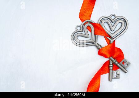 Close-up of two antique silver toned keys wrapped together with a red ribbon on a neutral background with copy space. Strong long lasting marriage cre Stock Photo