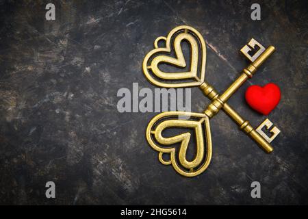 Crossed retro style gold-toned keys with a small red heart on a dark grungy table. Romantic devotion and loyalty concept. Stock Photo