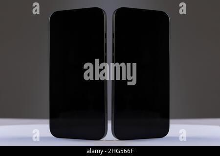 two black rectangular smartphones with glossy screens next to each other on a gray isolated background, concept mockup Stock Photo