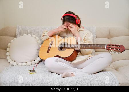 A shamed crying woman with acoustic guitar sitting on a bed in a home living room Stock Photo