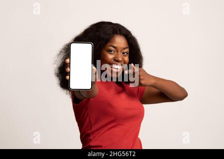 Check This Ad. Cheerful Black Woman Holding And Pointing At Blank Smartphone Stock Photo