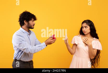 Declining proposal. Indian woman refusing to take engagement ring rejecting boyfriend, standing over yellow background Stock Photo