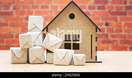 Pile of tiny packages in front of a miniature house model standing on the table against a brick wall background. Stock Photo