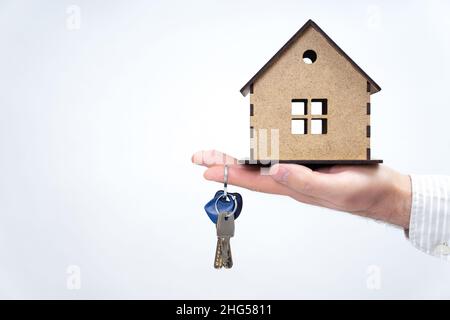 Close-up of a male hand holding keys and a wooden house model isolated on white background. Stock Photo