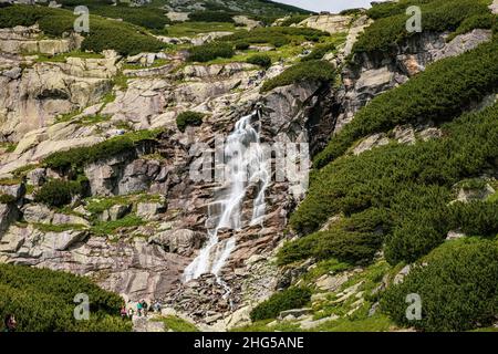 Beautiful waterfall with water stream falling from the mountain with green bushes Stock Photo