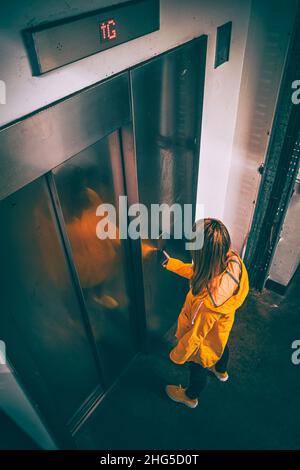 Woman wearing a yellow coat waiting for the lift in a car park Stock Photo