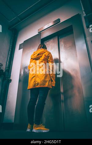 Woman wearing a yellow coat waiting for the lift in a car park Stock Photo