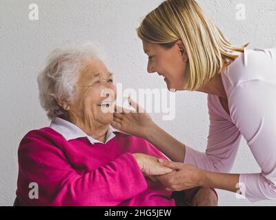 ELDERLY LADY with young caring carer visitor woman affectionately tactile touching hands cheek greeting charming happy smiling elderly senior old aged retired lady in natural light Stock Photo