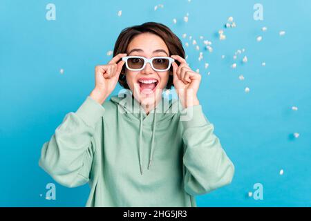 Photo of sweet excited woman wear green sweatshirt arms sunglass flying popcorn isolated blue color background Stock Photo