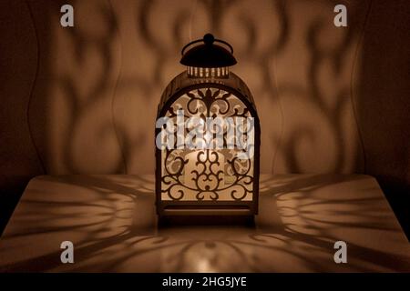 Ornamental lantern with burning candle. Decorative shadows. Festive table composition at night. Stock Photo