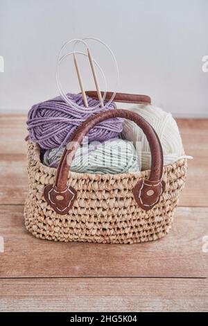 Skeins of yarn, wooden circular knitting needles in handmade straw basket on wooden table Stock Photo