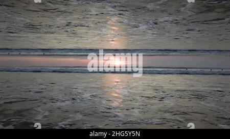 Stunning sunset sky above the ocean with a mirror horizon effect, view from the shore. Endless waves and people in water, inception theme Stock Photo