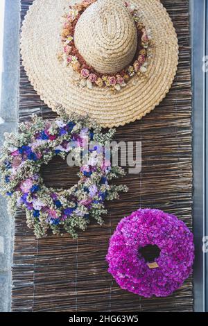 Spring wreaths of dried flowers of purple and pink flowers in a decoration and flower shop. On the wall weighs hat of straw decorated with a wreath of Stock Photo