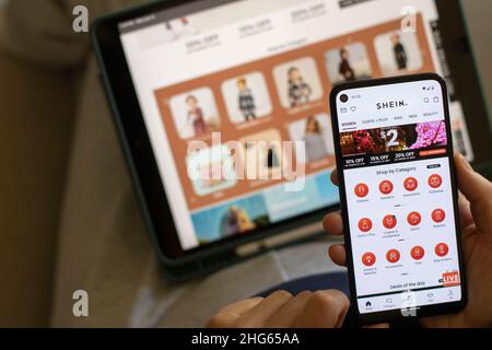 A woman shops kid's clothes via the SHEIN app on her phone. Shein is a Chinese online fast fashion retailer known for its affordably priced apparel. Stock Photo