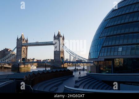 London, Greater London, England, January 5th 2022: |Woman walks in front of City Hall on a winters morning with double decker buses on Tower Bridge. Stock Photo