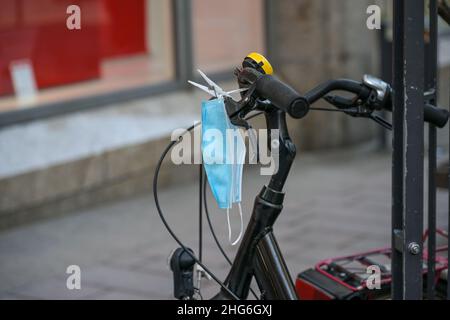 Surgical face mask hanging with a clothespin on a bicycle handlebar ready to be used in the city, protection against covid-19 infection during coronav Stock Photo