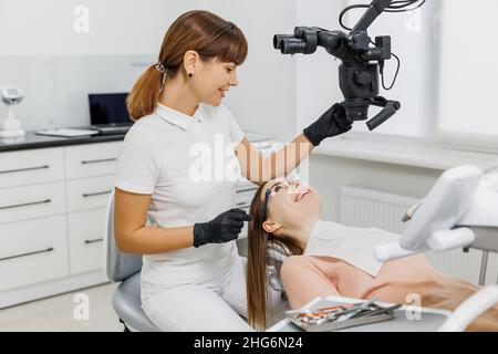 Friendly dentist talking to patient during teeth examination with microscope. Modern dental clinic. Concept of innovative equipment in oral treatment, health care. Stock Photo