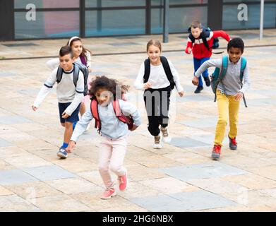 Group of cheerful tweenagers running in school yard after lessons Stock Photo