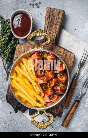 Traditional German currywurst sausage, served with chips or French fries in a pan. Gray background. Top view Stock Photo